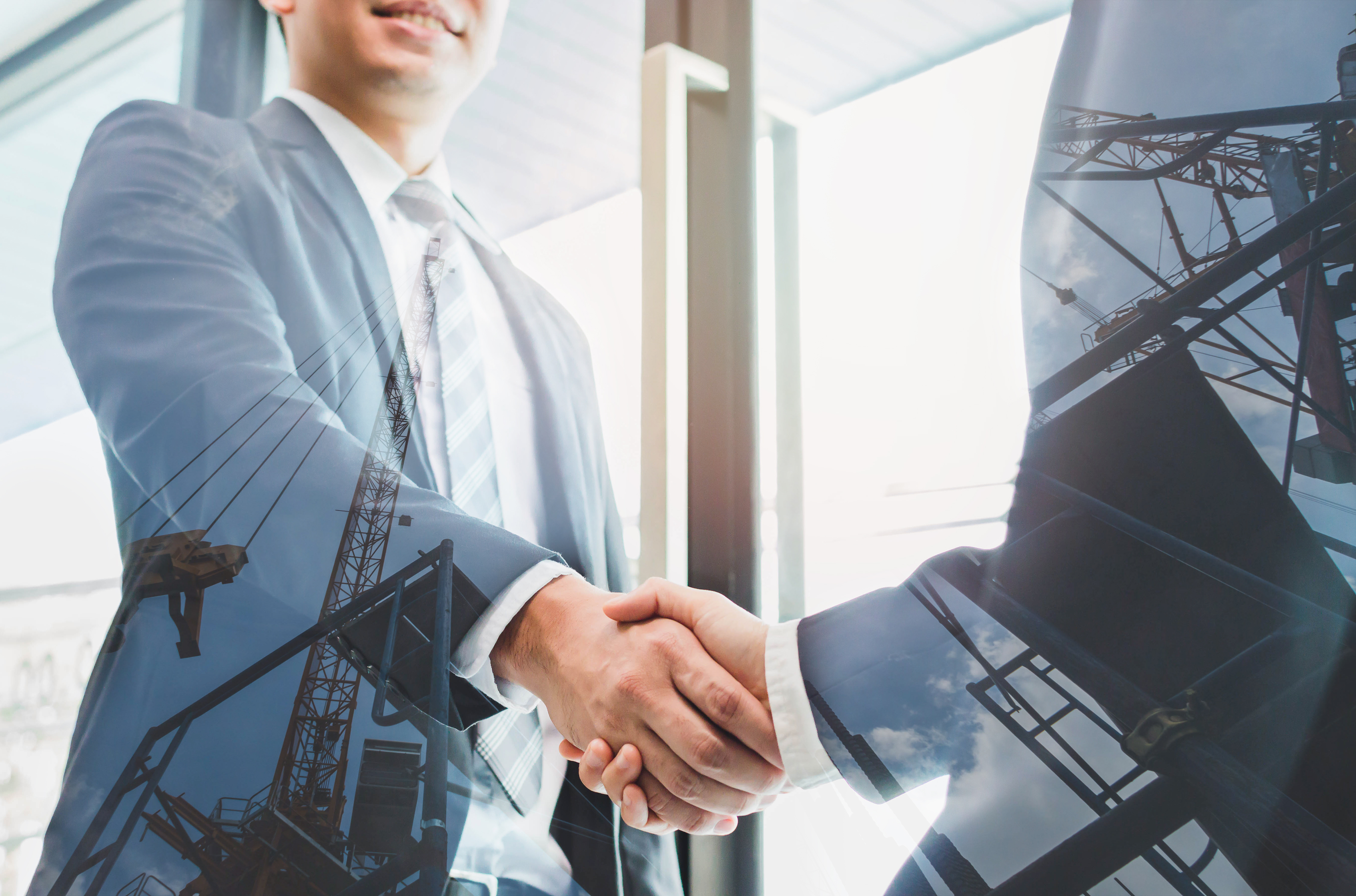 Double exposure of two businessmen reaching an agreement and making handshake with abstract construction site